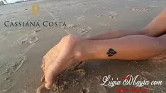 Reproducir Ella está parada sin sostén en la playa sobre la arena caliente.